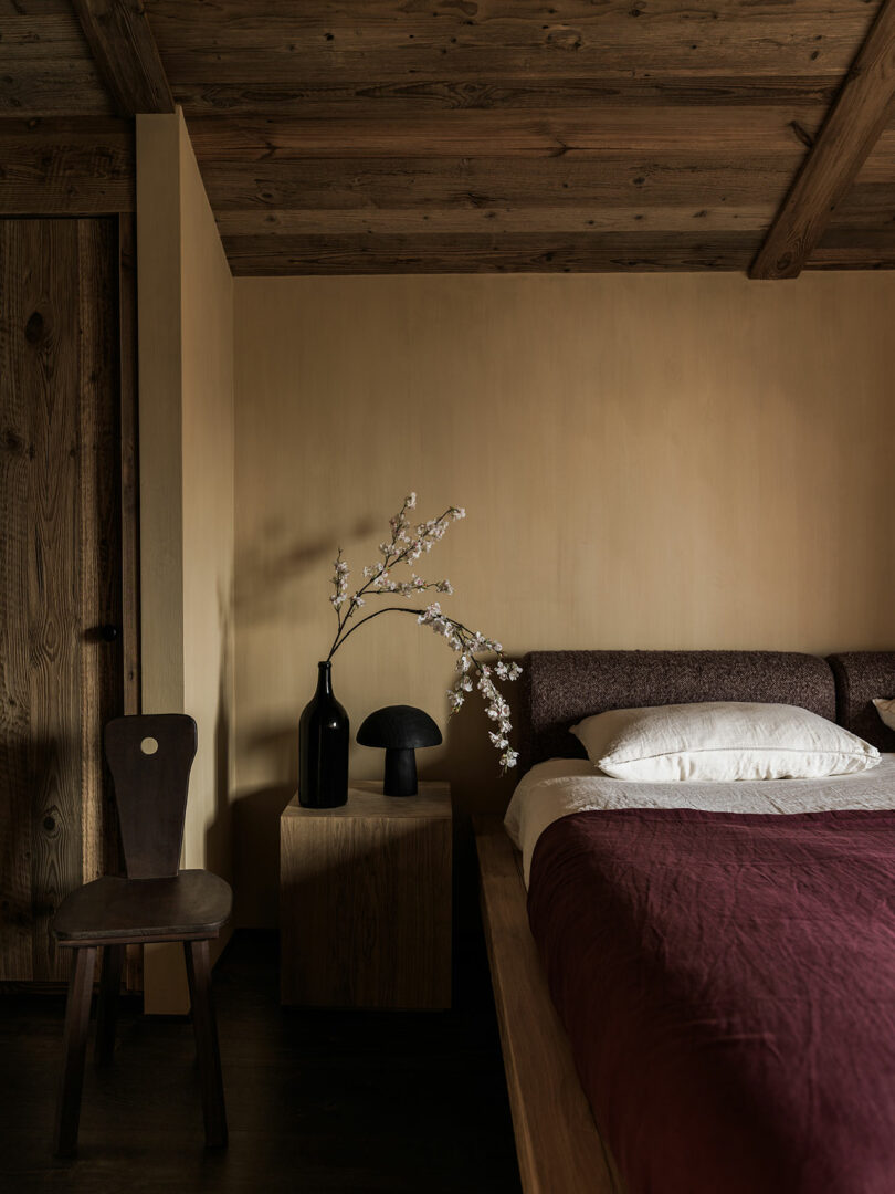 A minimalist bedroom featuring a deep burgundy bedspread against natural wood walls and ceiling.