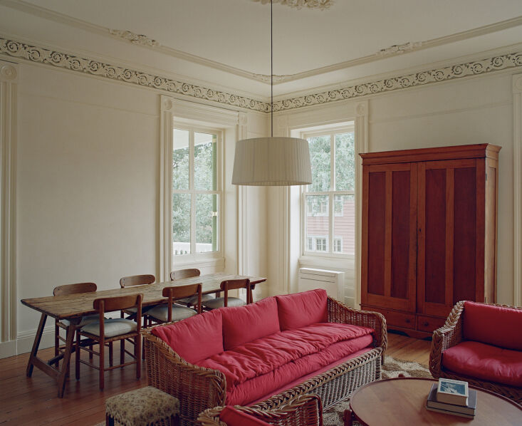 A living room featuring Tallow-colored walls, wicker furniture, and vibrant red upholstery.