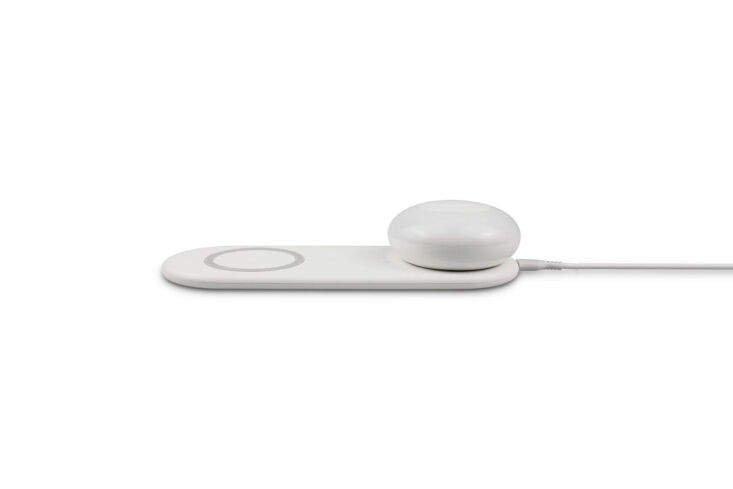 A minimalist white bedside lamp with a smartphone resting on its wireless charging base.