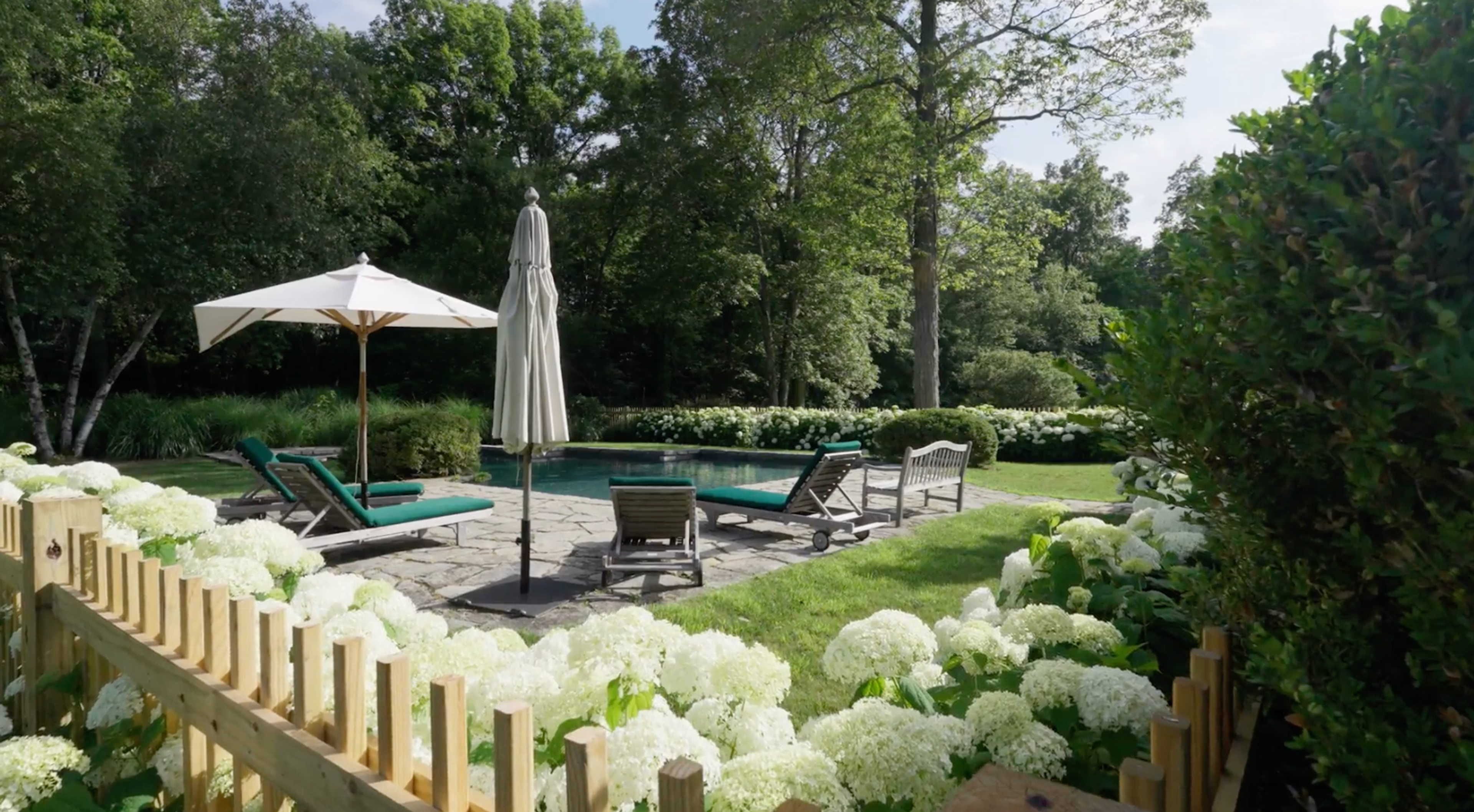 An outdoor swimming pool surrounded by a minimalist stone deck and lush trees.