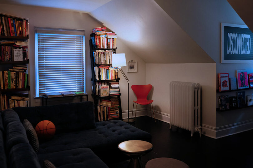 A cozy, well-lit attic reading room with bookshelves, a red chair, and framed art.
