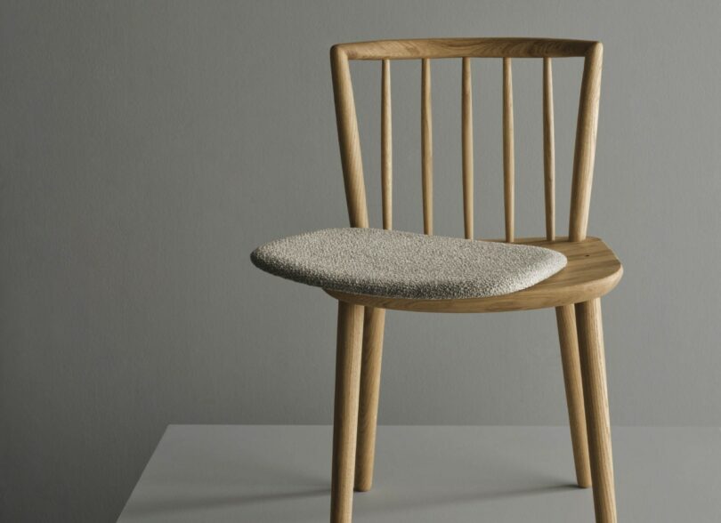A wooden chair with vertical slats and a light gray cushion against a neutral background.