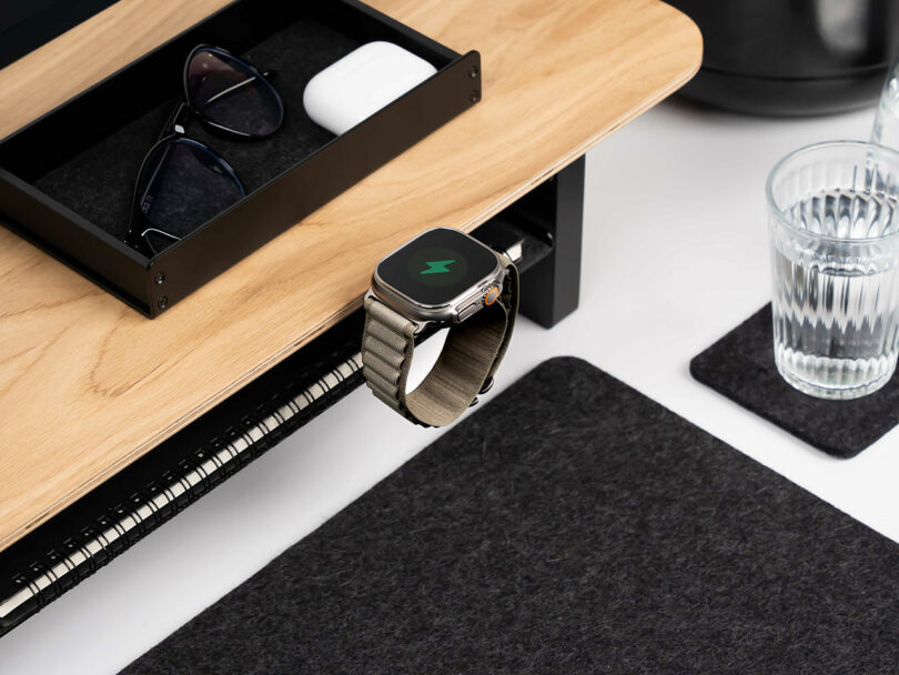 A smartwatch charging on a Balolo mount next to a small wooden drawer accessory.