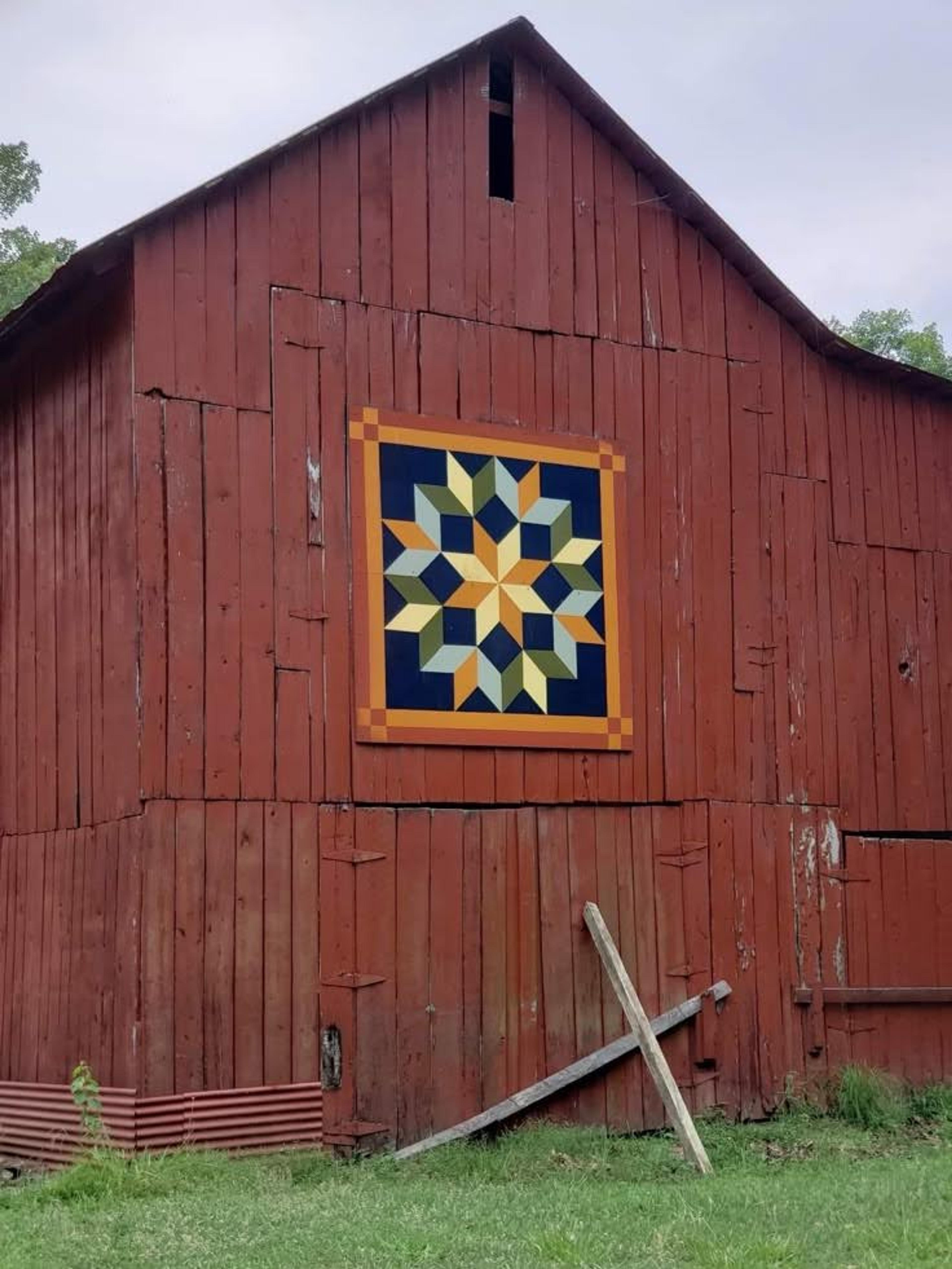 A classic bright red barn featuring a large geometric quilt pattern on its exterior wall.