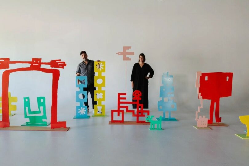 Amanda Jane Jones and a colleague in a studio surrounded by large-scale colorful abstract sculptures.