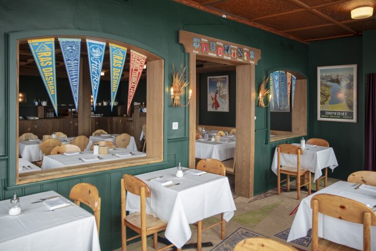 The hotel restaurant with forest green walls, custom wooden tables, and traditional Tyrolean chairs.
