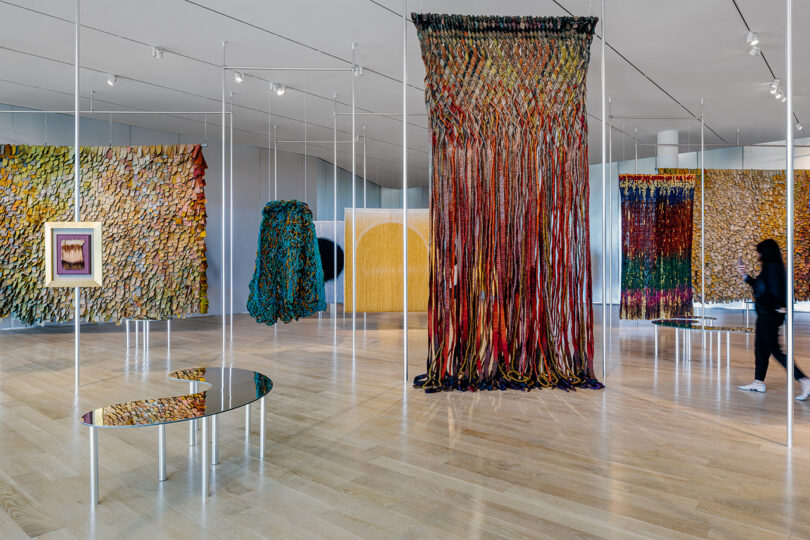A person walking through a gallery filled with colorful textile installations and mirrored furniture.