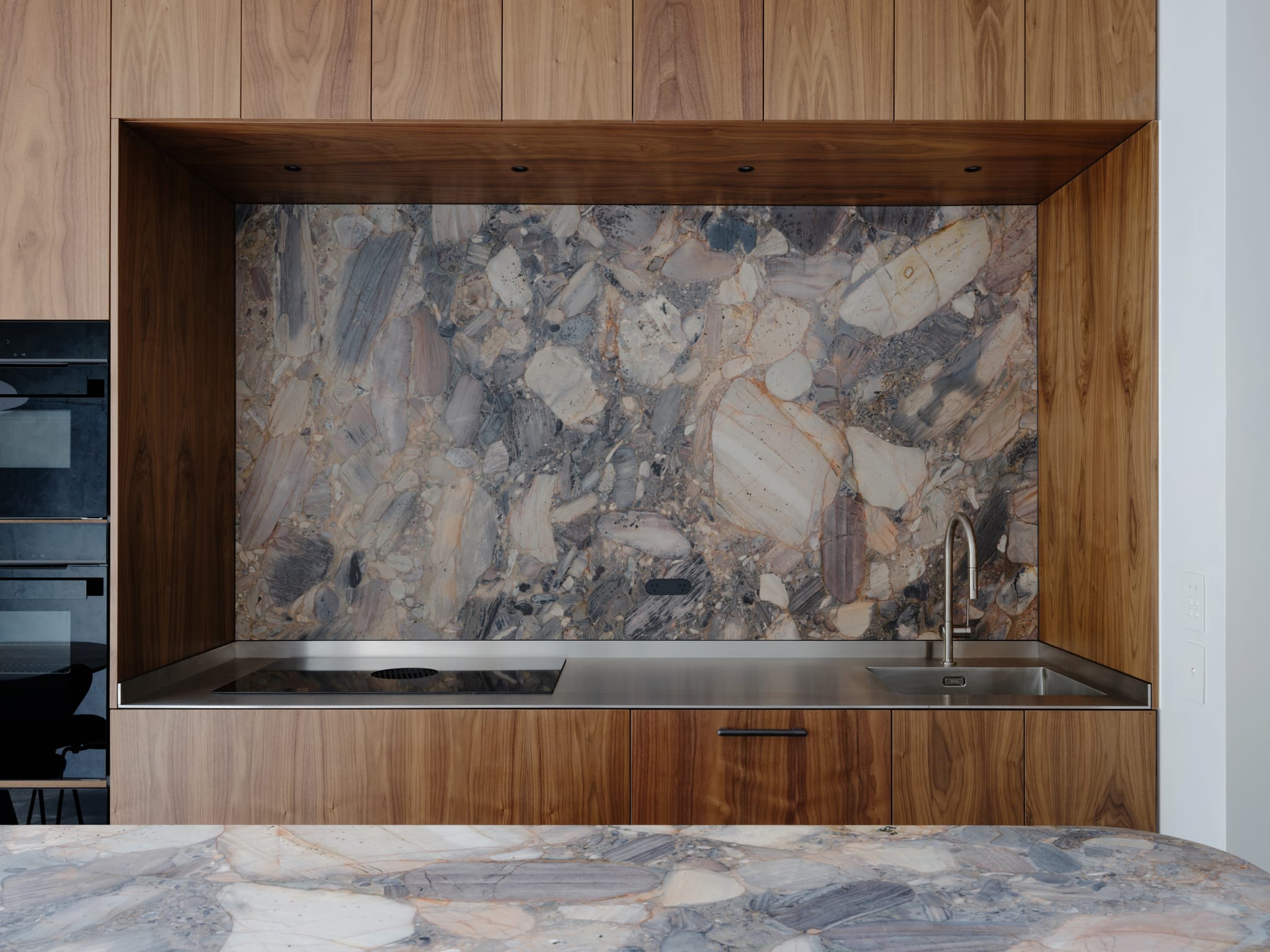 Close-up of the kitchen or bathroom featuring natural stone, concrete, and walnut timber joinery.
