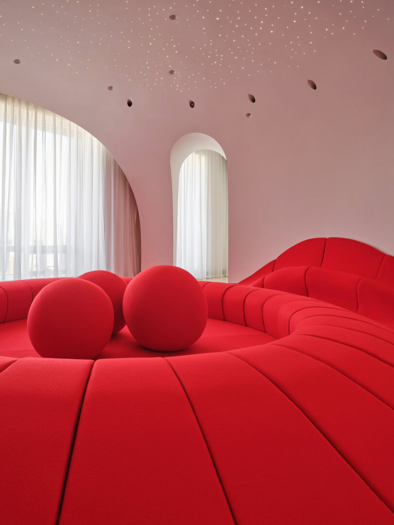 A modern room featuring a curved red sofa, spherical cushions, and star-like ceiling lights.
