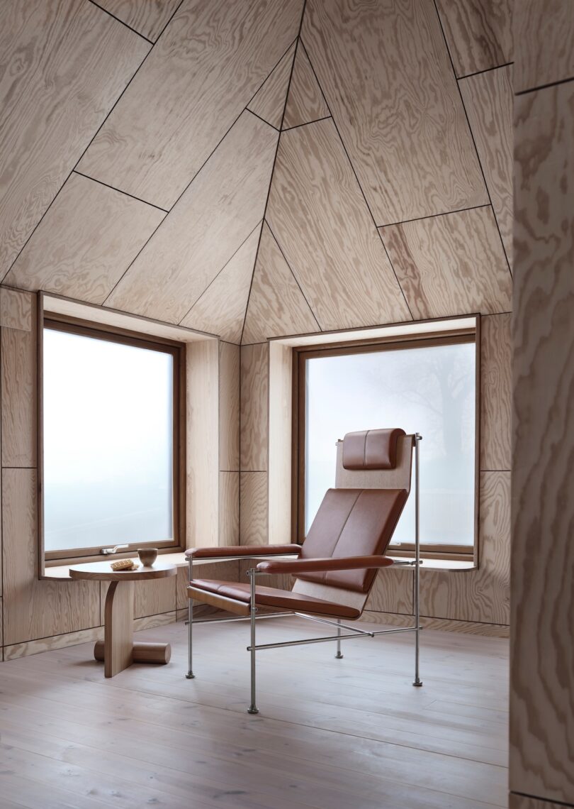 Brown leather Villhem chair with a headrest and metal frame in a sunlit room with wooden walls.