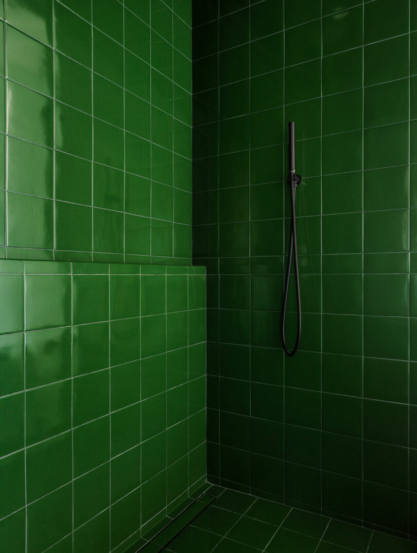 A walk-in shower with vibrant green vertical tiles and minimalist black fixtures.