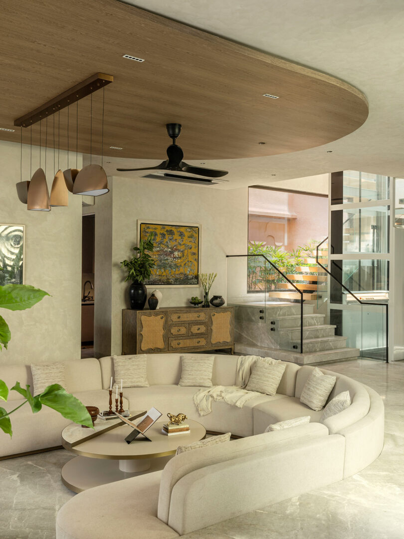 An open-plan living room featuring a curved beige sectional sofa and a view of the glass-railed staircase.