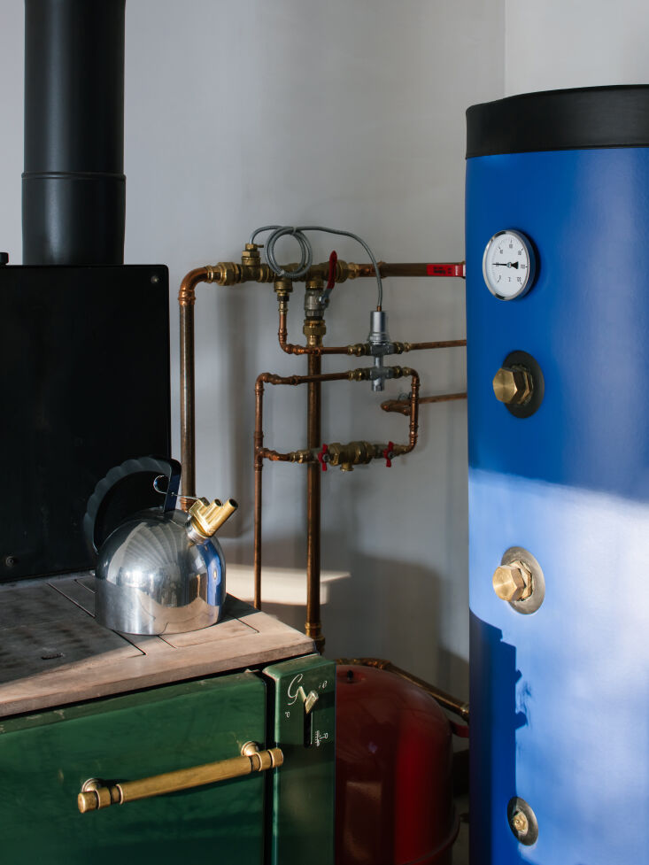 A modern wood-fired boiler stove connected to cast-iron radiators inside the house.