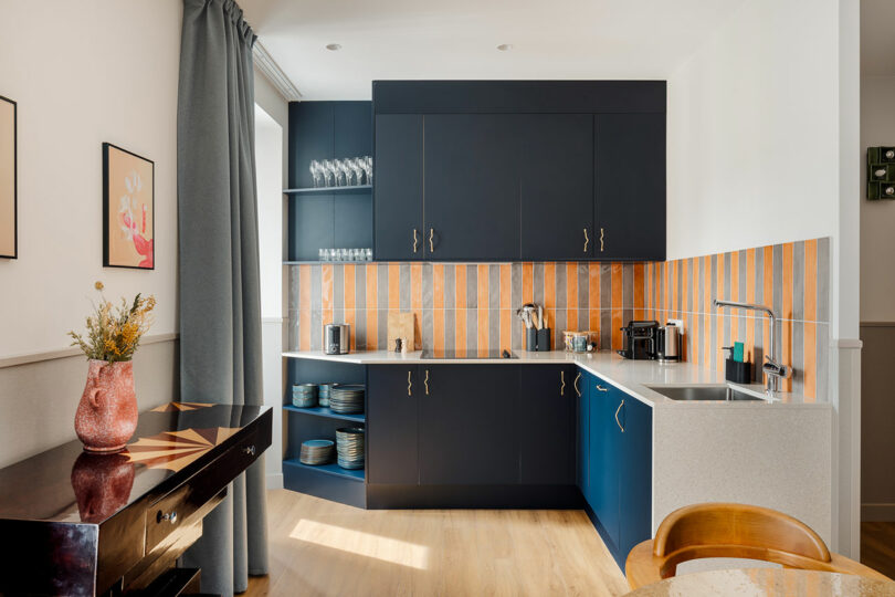 Modern kitchen with dark blue cabinets and a vibrant orange-striped tile backsplash.