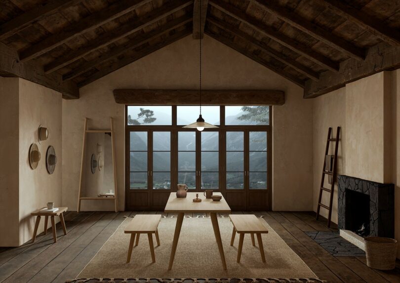 A rustic dining room with high wooden beams, a long table with matching benches, and a view of mountains through large windows.