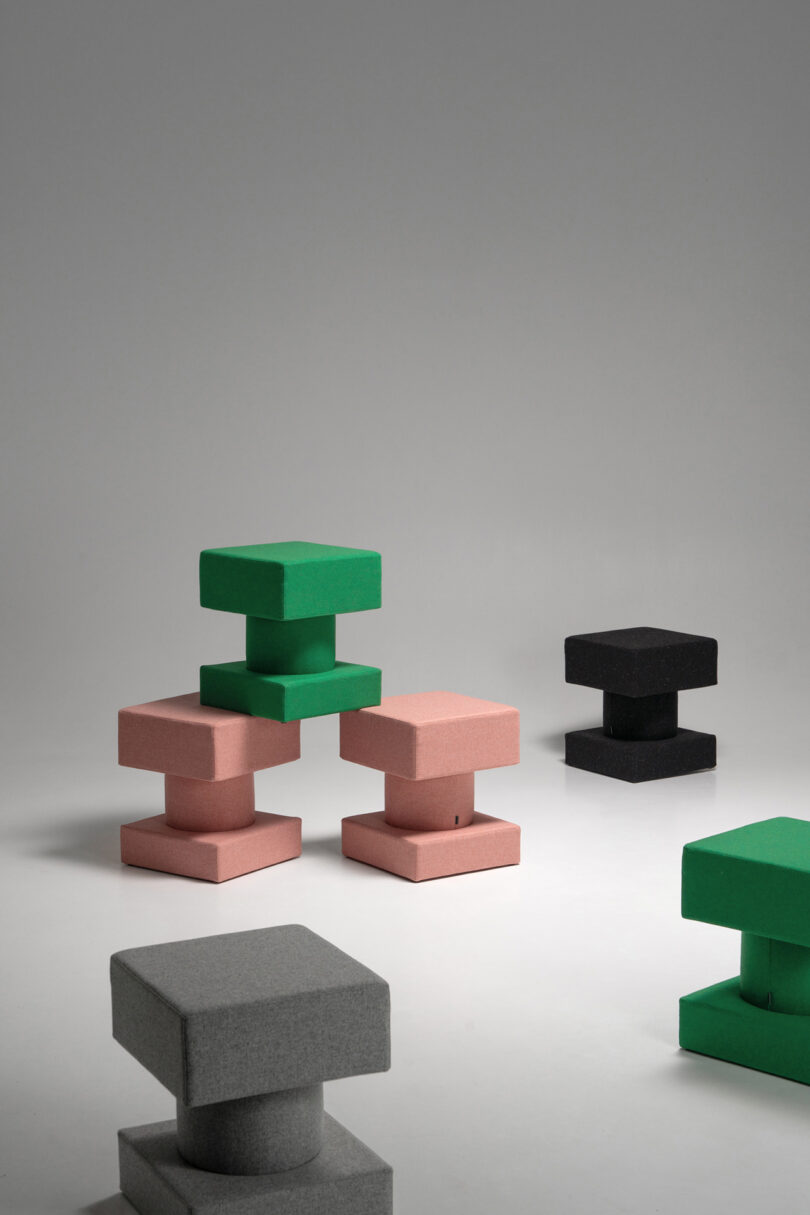 A group of TAITŌ stools in green, pink, black, and gray arranged on a neutral surface.