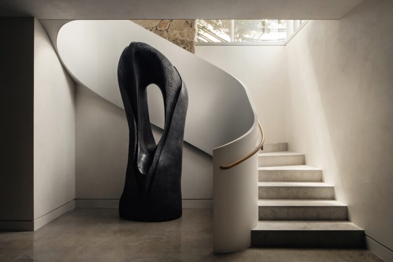 A minimalist white spiral staircase curving around a tall black abstract sculpture.