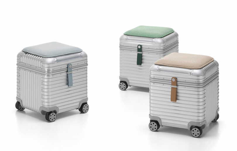 Three metallic wheeled storage boxes with ribbed surfaces and cushioned tops in blue, green, and beige.