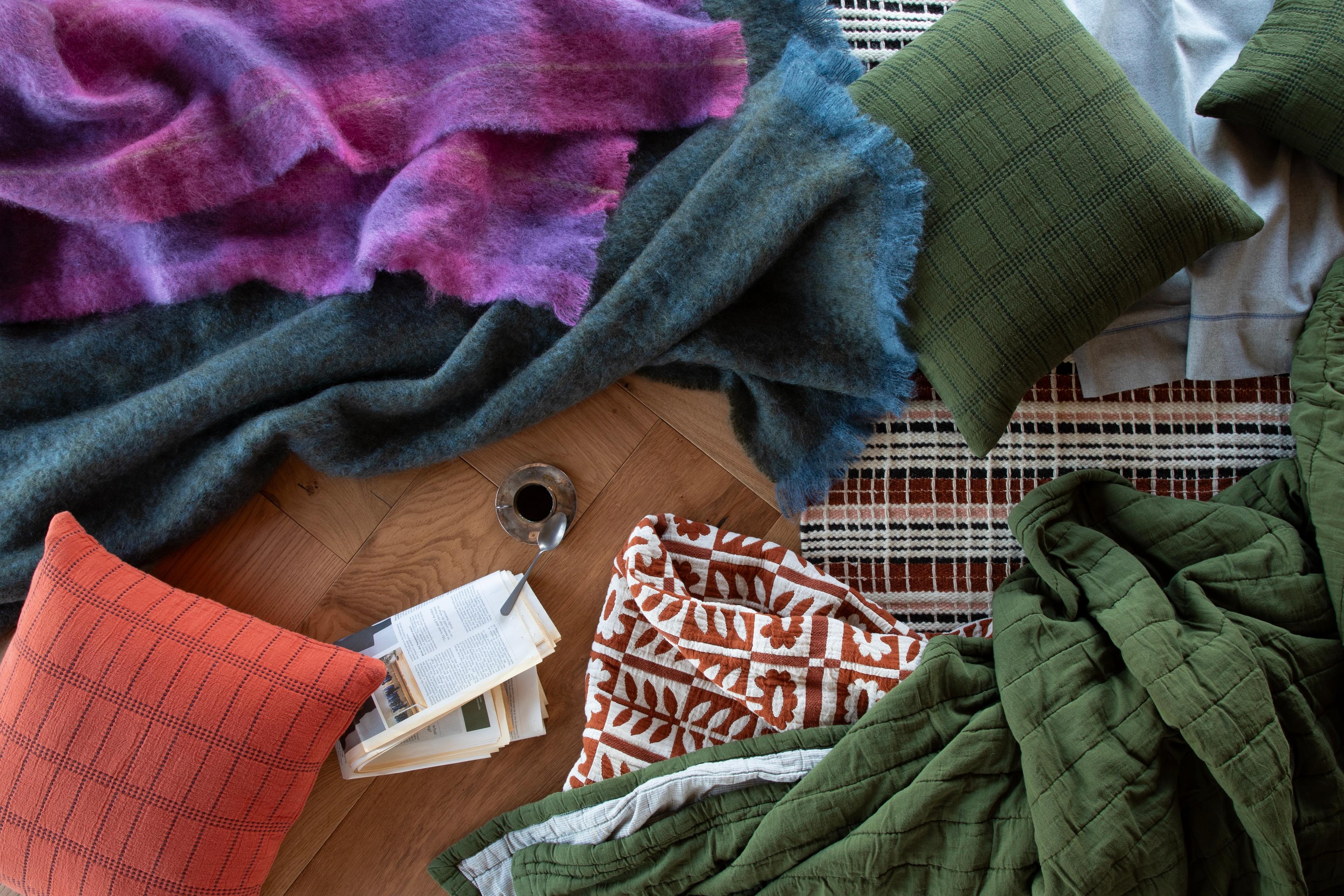 Cozy interior scene with stacked blankets and pillows in neutral tones.