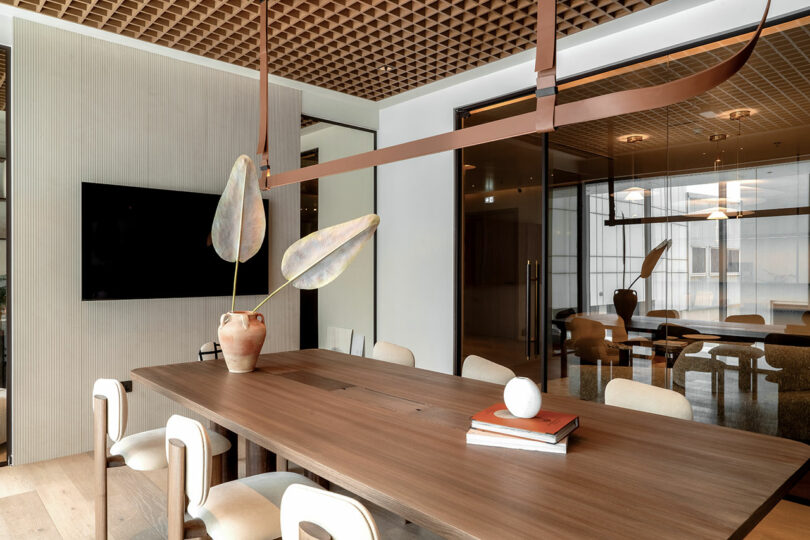 Modern conference room with a large wooden table, grid ceiling, and integrated TV display.