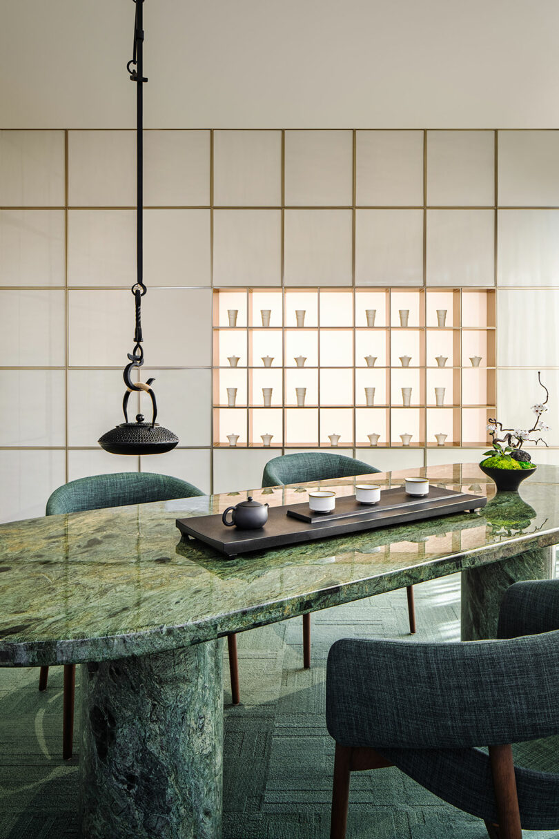 A green marble dining table with modern chairs in a minimalist, backlit setting.