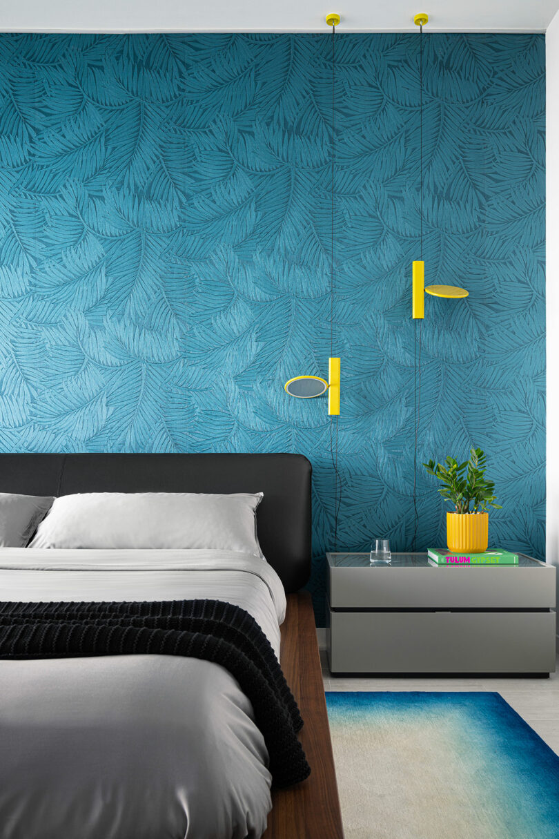 Bedroom with teal leaf-patterned wallpaper, gray bedding, and modern yellow wall lamps.