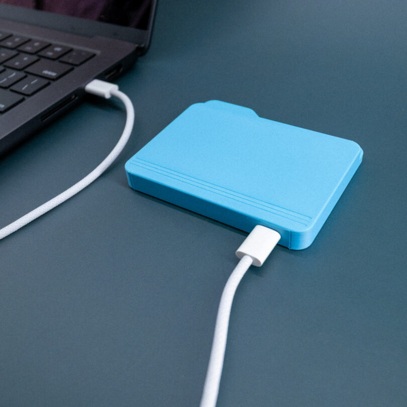 A blue folder-shaped external drive placed on a matching blue surface next to a laptop.