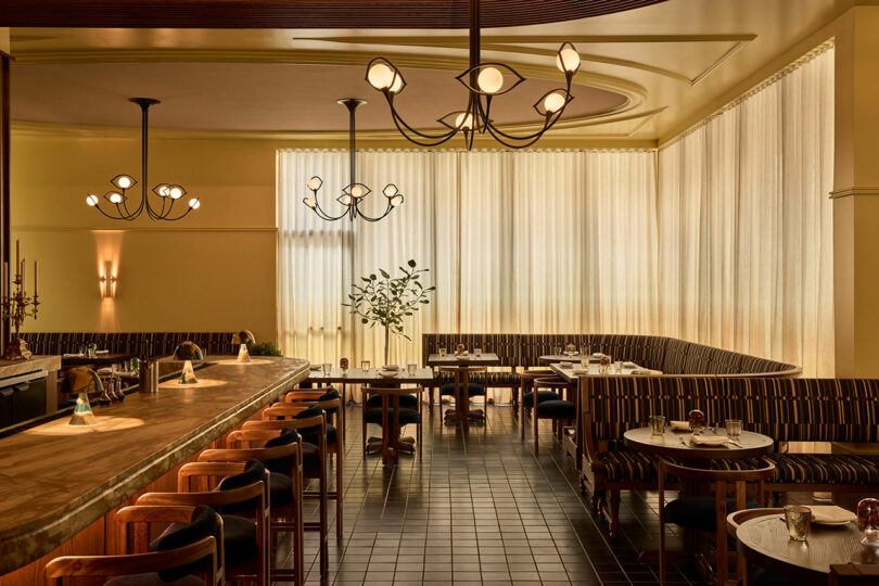 The interior of a modern restaurant with a long bar, wooden furniture, and warm lighting.