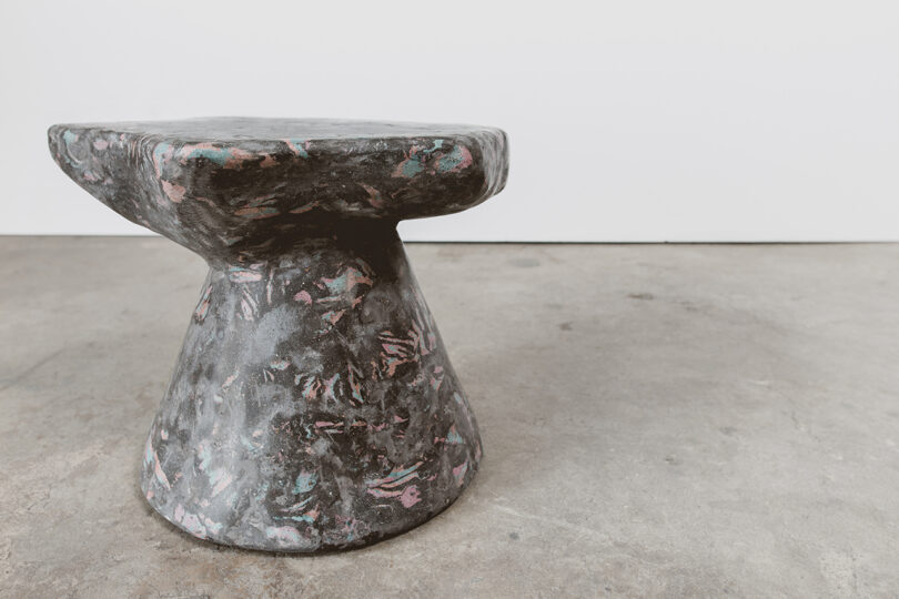 A conical dark marbled stool with pink veining on a concrete floor.