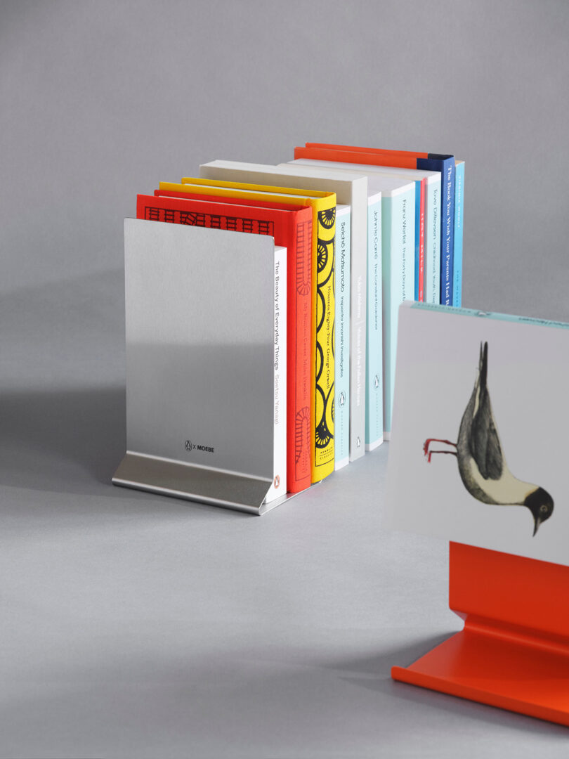 A row of colorful books held upright by a silver stand and an orange stand with a bird illustration.