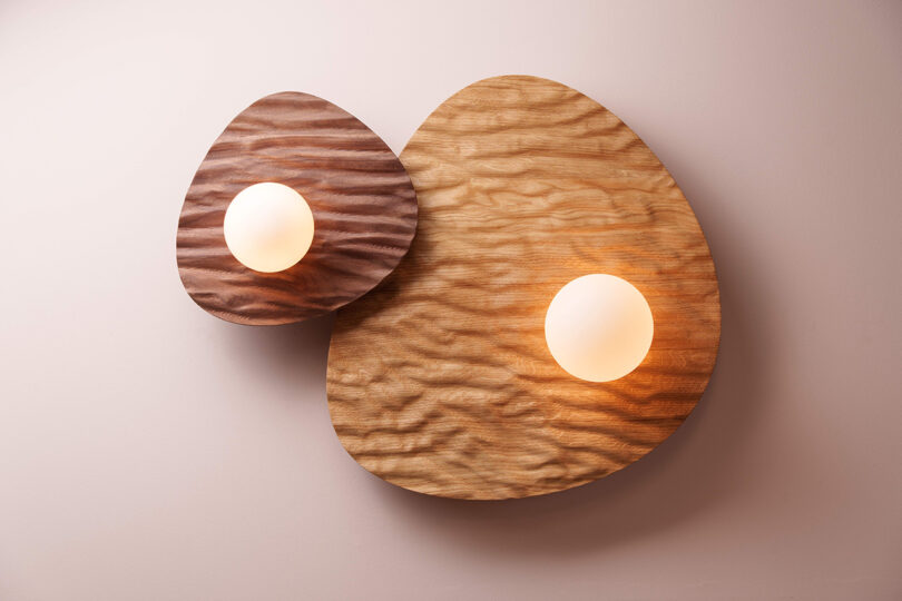 Two irregularly shaped wall lights with overlapping textured wooden panels on a light wall.