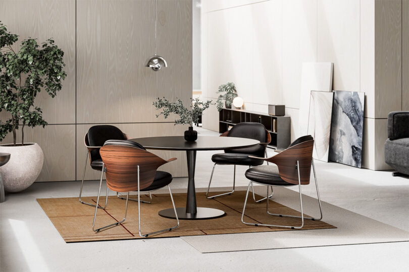 A bright, open dining and living area featuring modern chairs and a round black table on a brown rug.