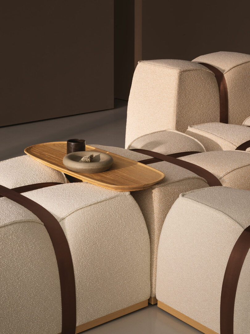 Close-up of beige modular seating with brown straps and a wooden tray holding a ceramic cup.