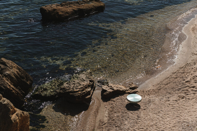 A serene beach landscape with clear water and a green umbrella, echoing the colors of the Seahorse Table.