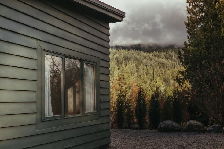 The cabin viewed from a dirt road with mountains in the background.