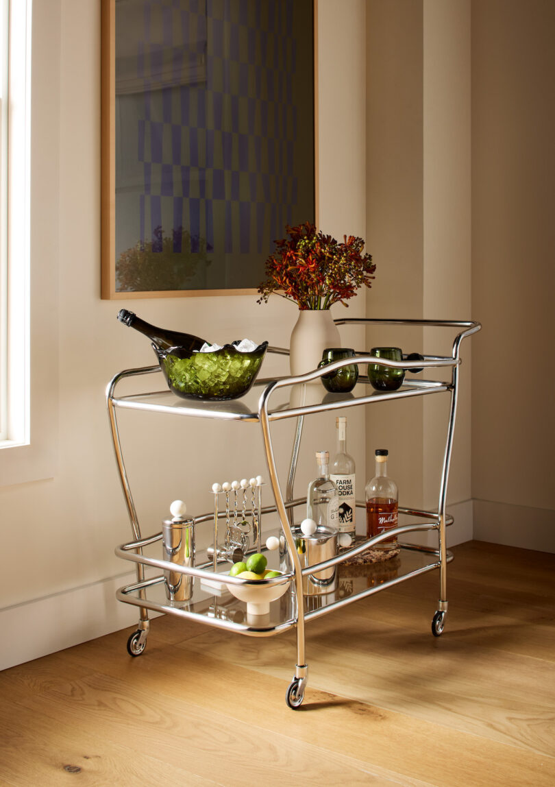 A chrome Freya Bar Cart styled with champagne, glassware, and bar tools against a large window.