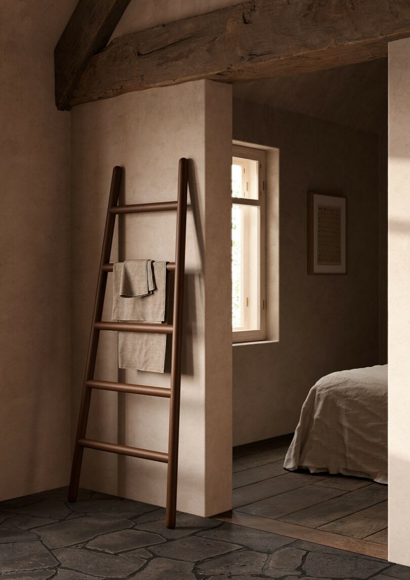 A wooden blanket ladder with towels in a minimalist bedroom with stone floors and natural light.