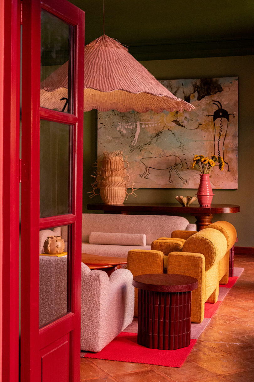 A vibrant living room with a red door frame, yellow sofa, and white armchairs arranged on a red rug.