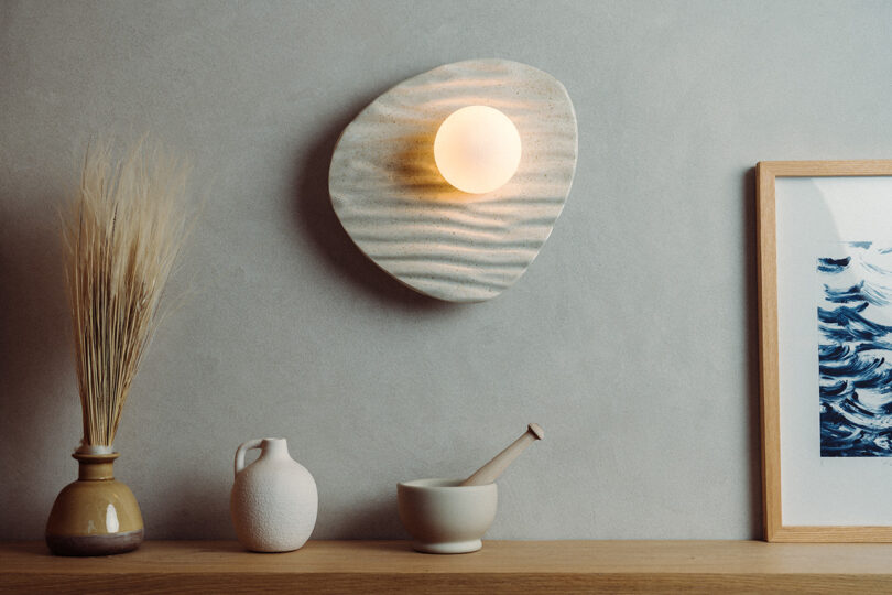 A modern wall sconce with deep, wavy wood textures illuminated by a central bulb.