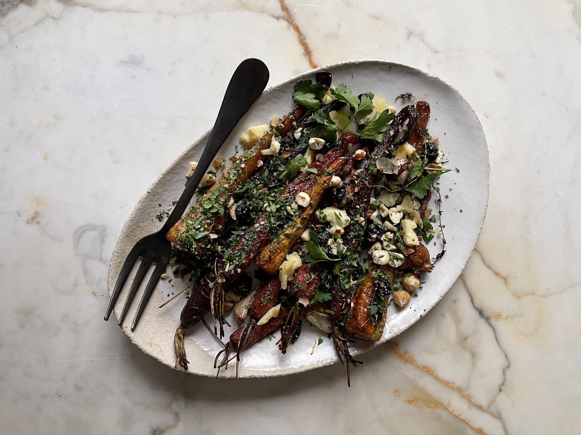 Close-up of roasted root vegetables featuring lemon zest, toasted hazelnuts, and crumbled English cheddar.