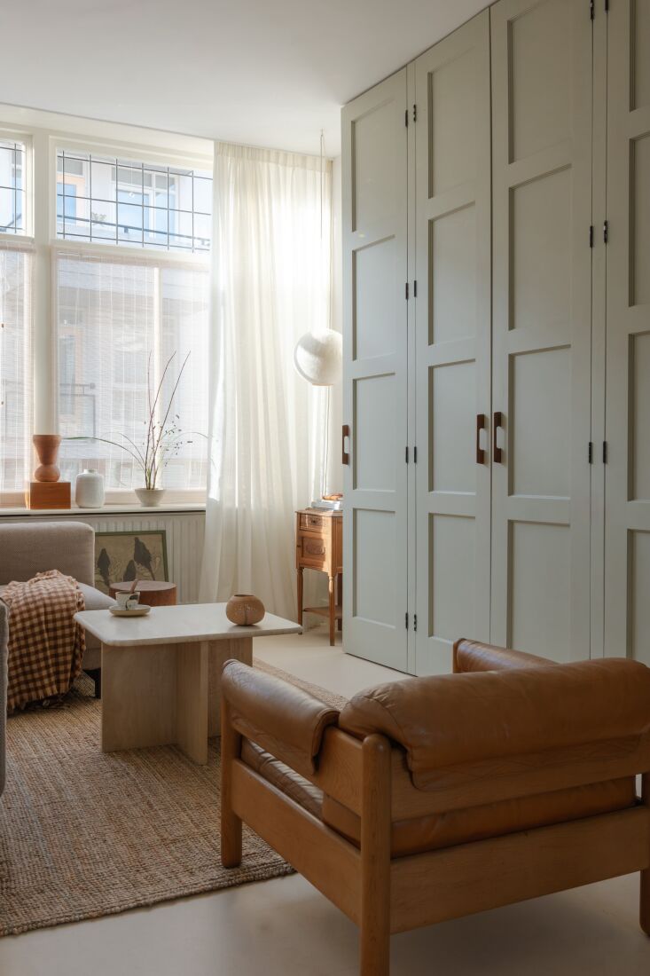 A large custom-built storage cabinet painted in soft grey with wooden handles, housing a TV.