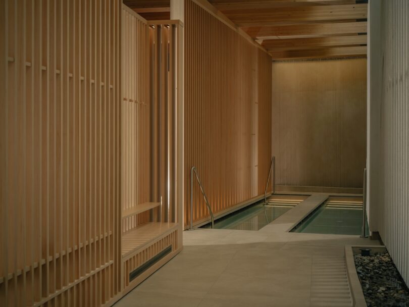 Indoor pool area featuring vertical wooden slats and a stone-bordered pool with metal handrails.