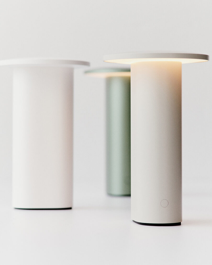 Three minimalist cylindrical table lamps in white and green finishes by Cecilie Manz.