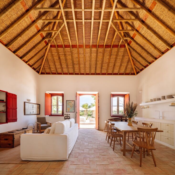 Interior of a converted barn showing an exposed rafter ceiling with straw and red interior shutters.