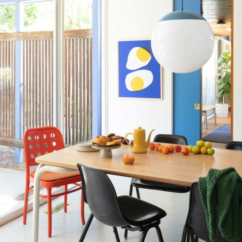 A modern dining and work area with colorful chairs, abstract art, and a yellow teapot.