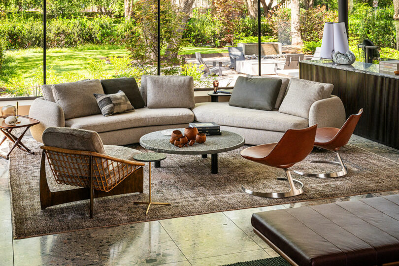 Modern living room with a curved beige sofa and floor-to-ceiling windows showing a lush garden.