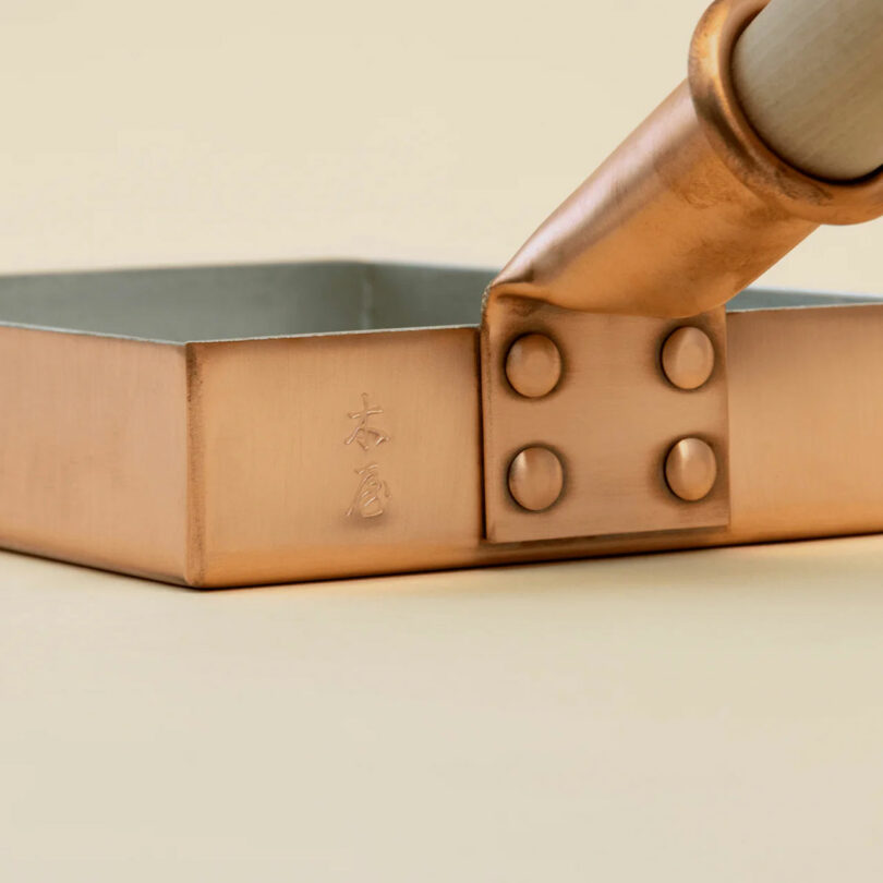 Close-up of a handcrafted square copper tamago pan with Japanese engravings and a sturdy riveted handle.