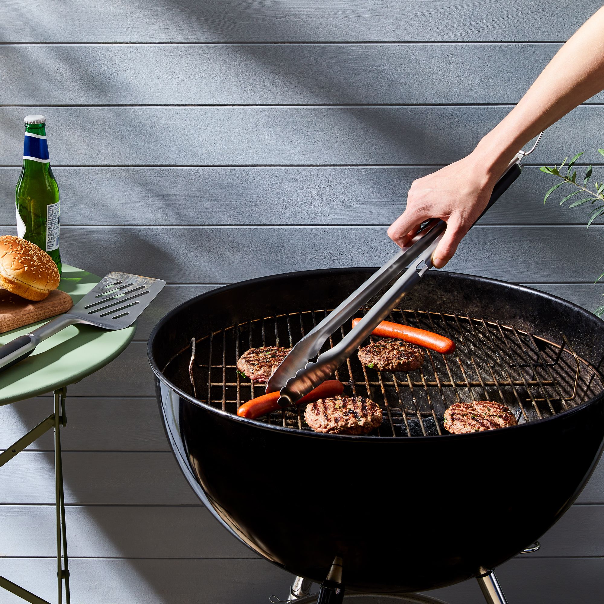 A close-up of a hand using a crumpled ball of aluminum foil to scrub residue off a warm stainless steel grill grate.