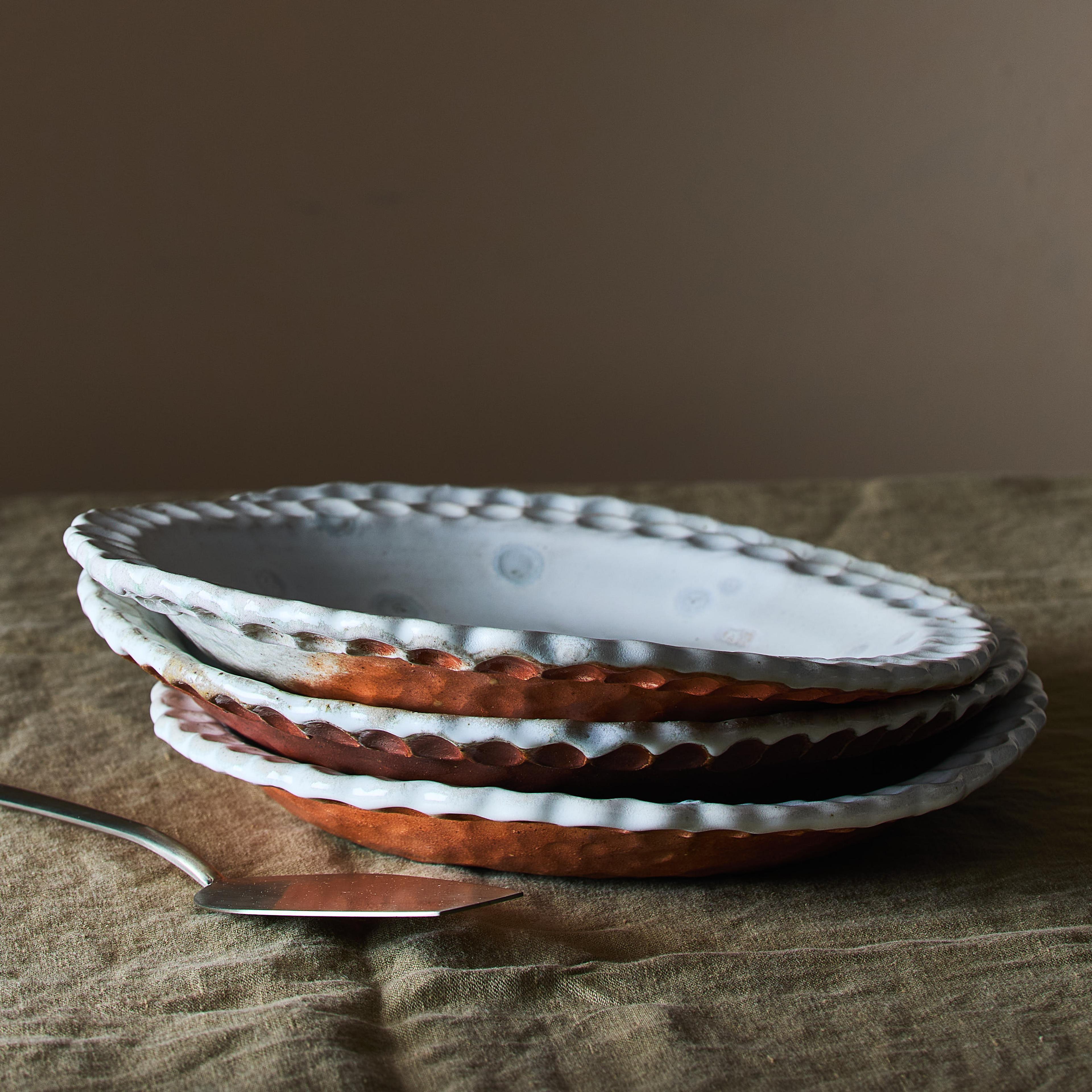 A stack of various wood-fired ceramic pie plates with different earthy patterns and textures.