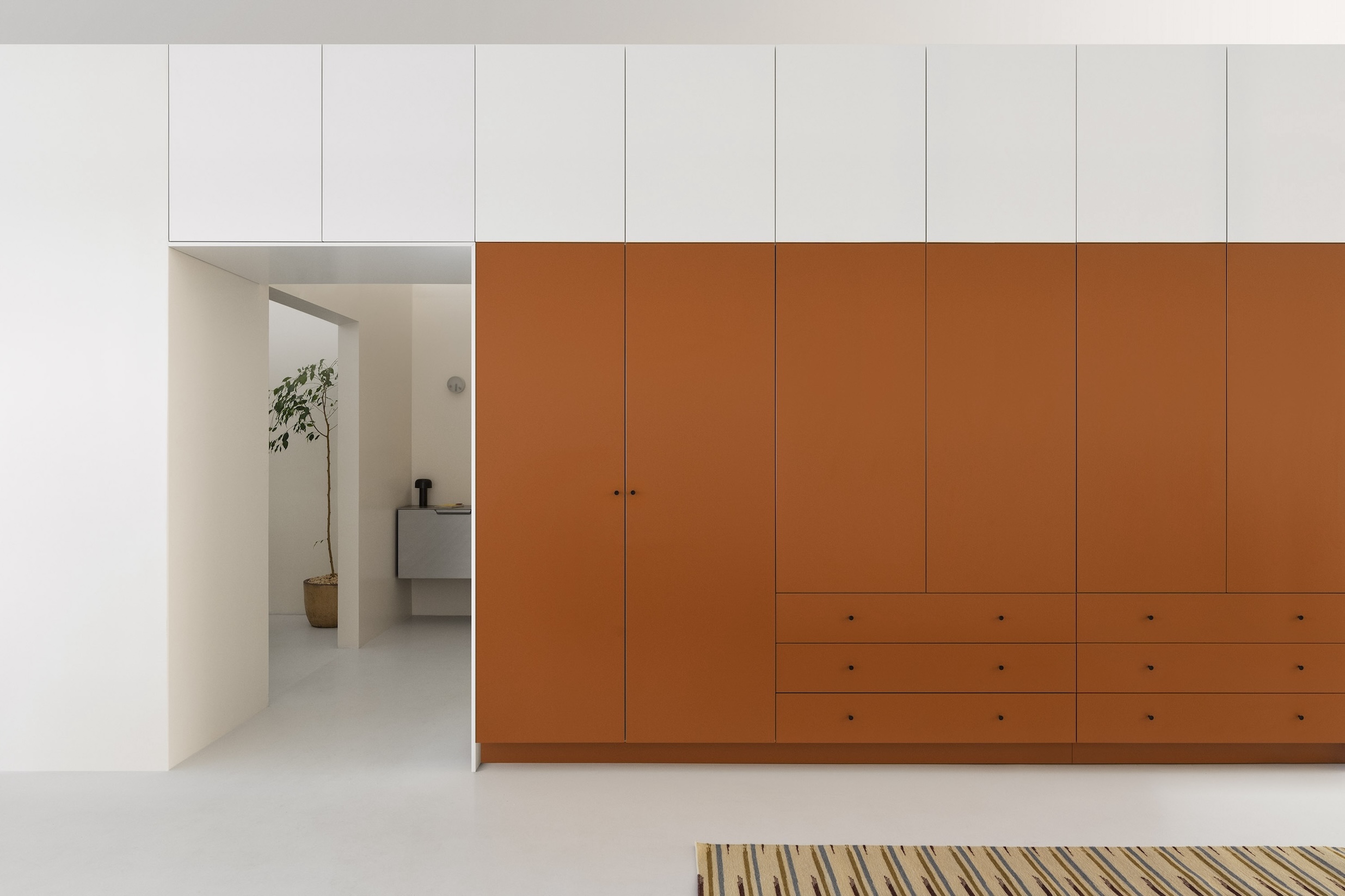 A wardrobe from the Plain collection in a Dusty Orange painted finish framing a doorway.